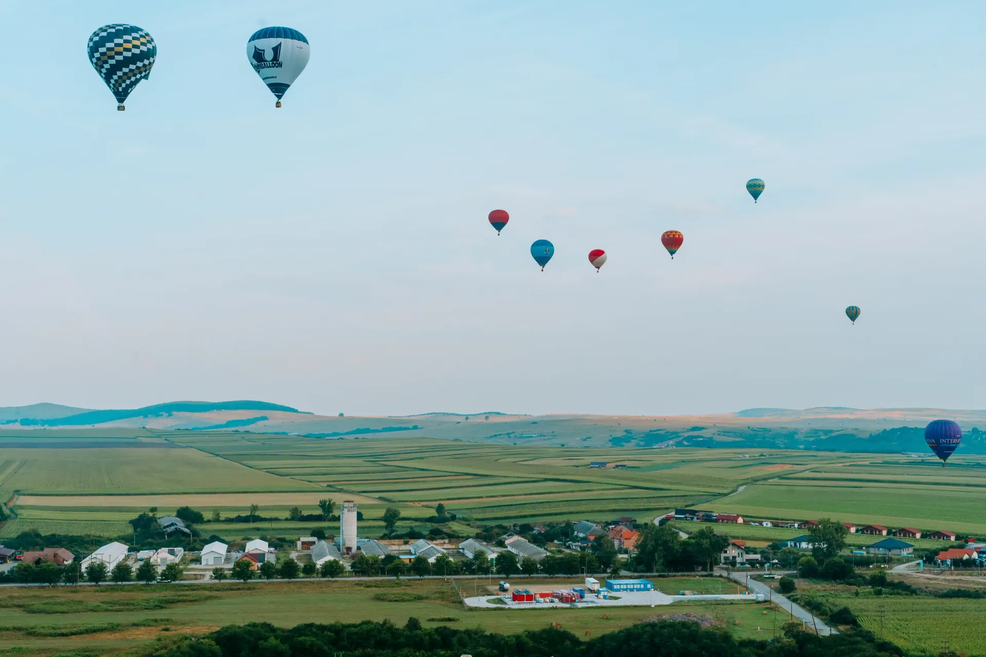 Baloane cu aer cald în zbor deasupra câmpurilor, văzute de la distanță